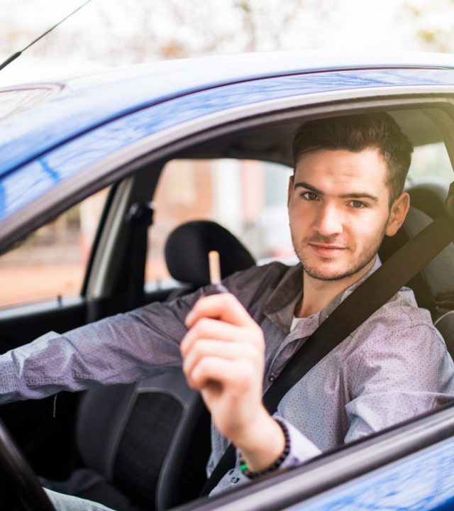 Young man driving his new car, holding out keys